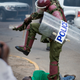 A Kenyan riot policeman repeatedly kicks a protester as he lies in the street.